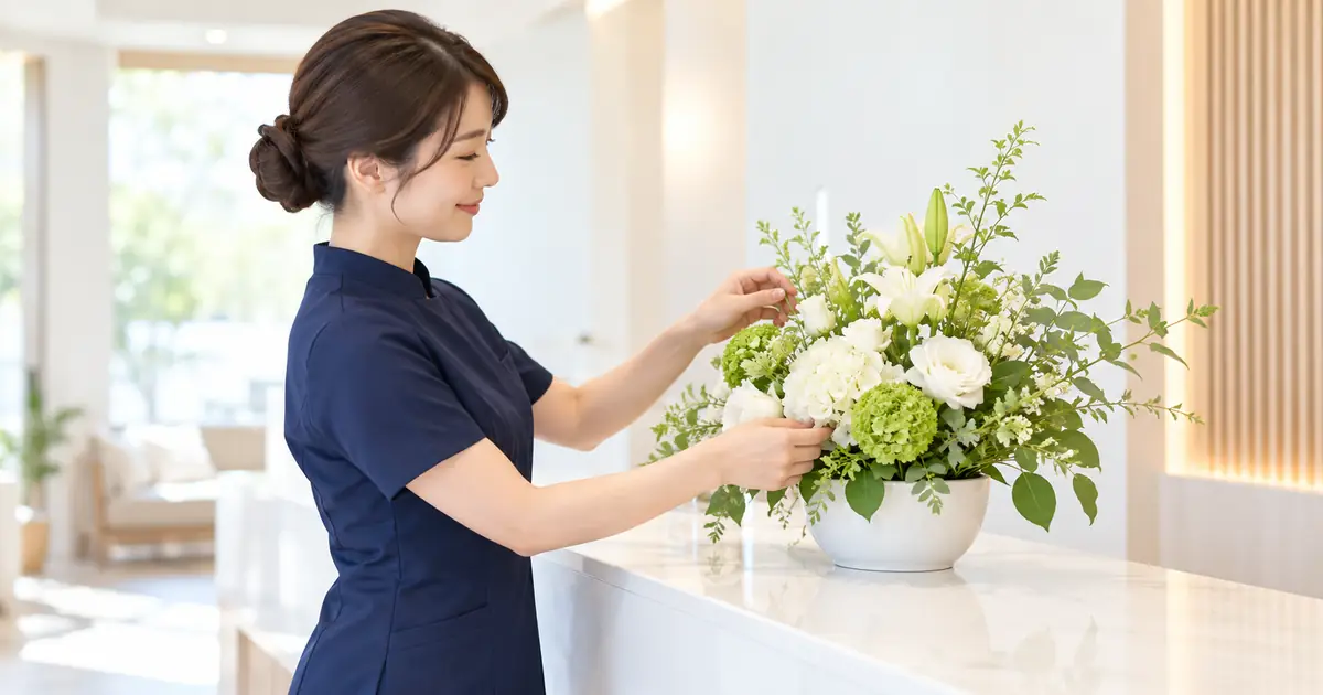 明るい真新しい受付で、紺の制服のセラピストが白と若草色の開店祝いの花をほほえみながら整えている横顔